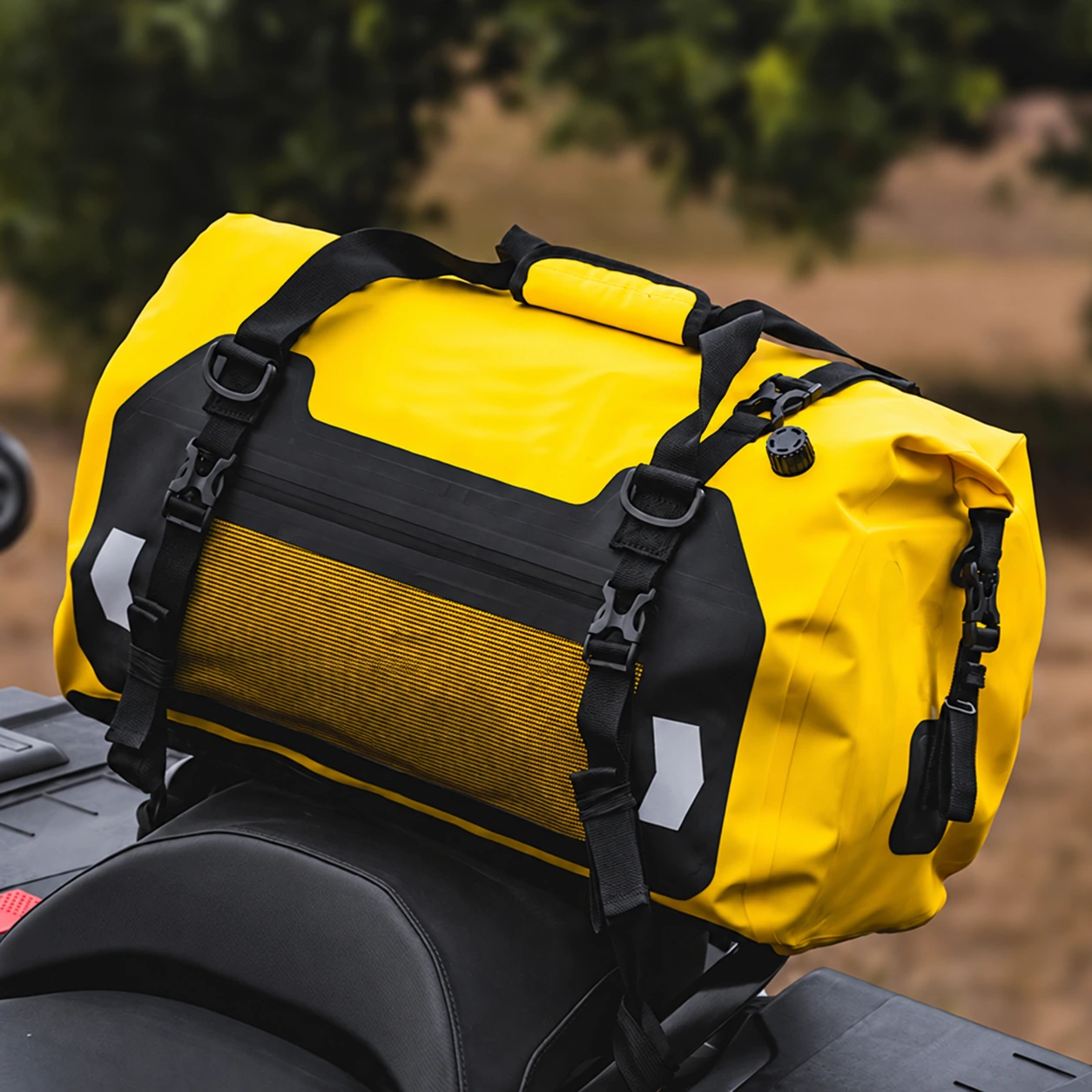 Yellow roll-top motorcycle luggage installed behind the seat, showing carry handles, buckle straps and mesh organisation